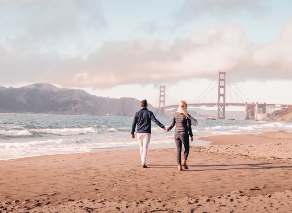 A couple walking on beach near the San Francisco bridge